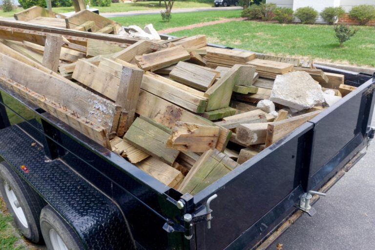Mixed renovation debris including lumber, drywall, broken concrete, roofing shingles, and demolition materials inside a dump trailer.